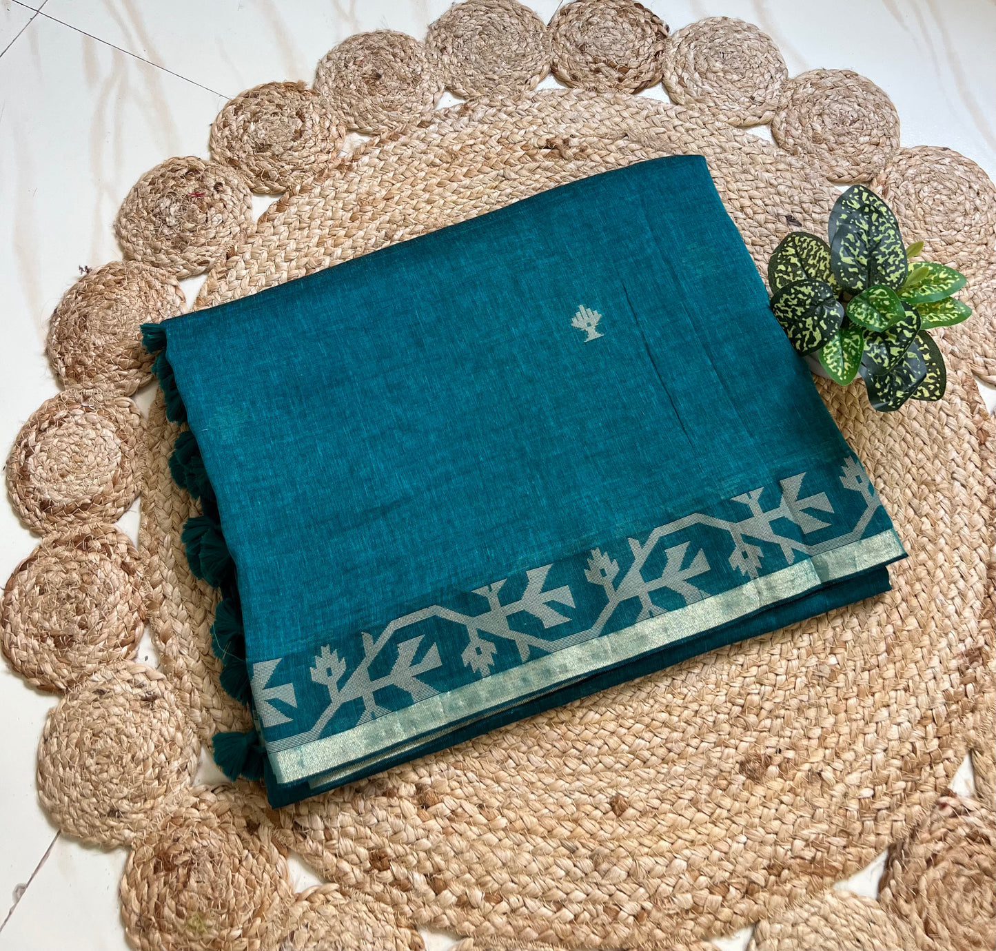 Folded peacock blue cotton jamdani saree showing woven border and motifs