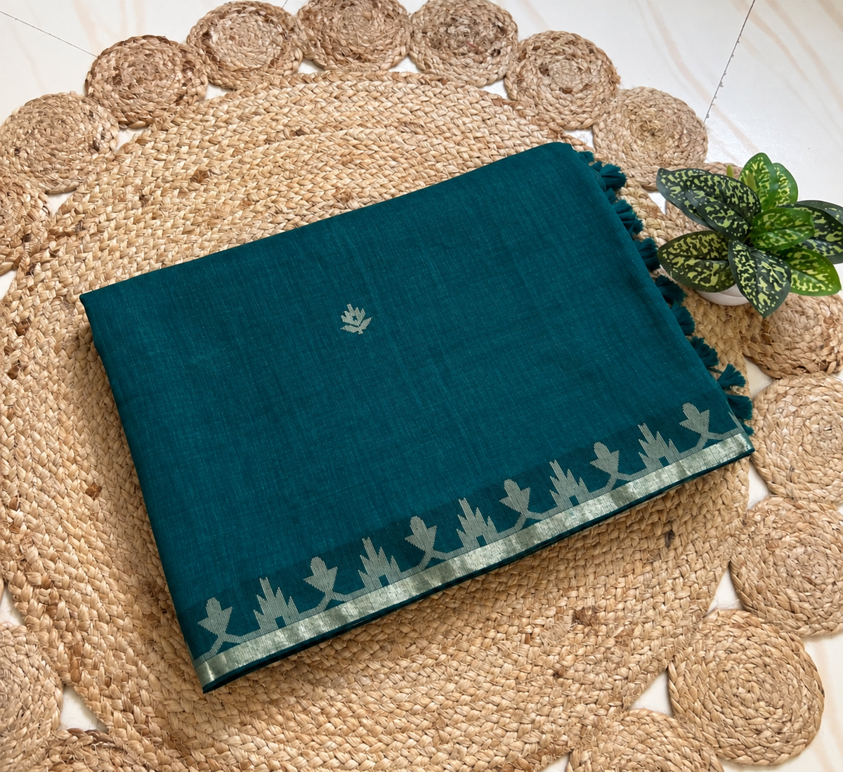 Folded deep teal cotton jamdani saree showing woven border and motifs
