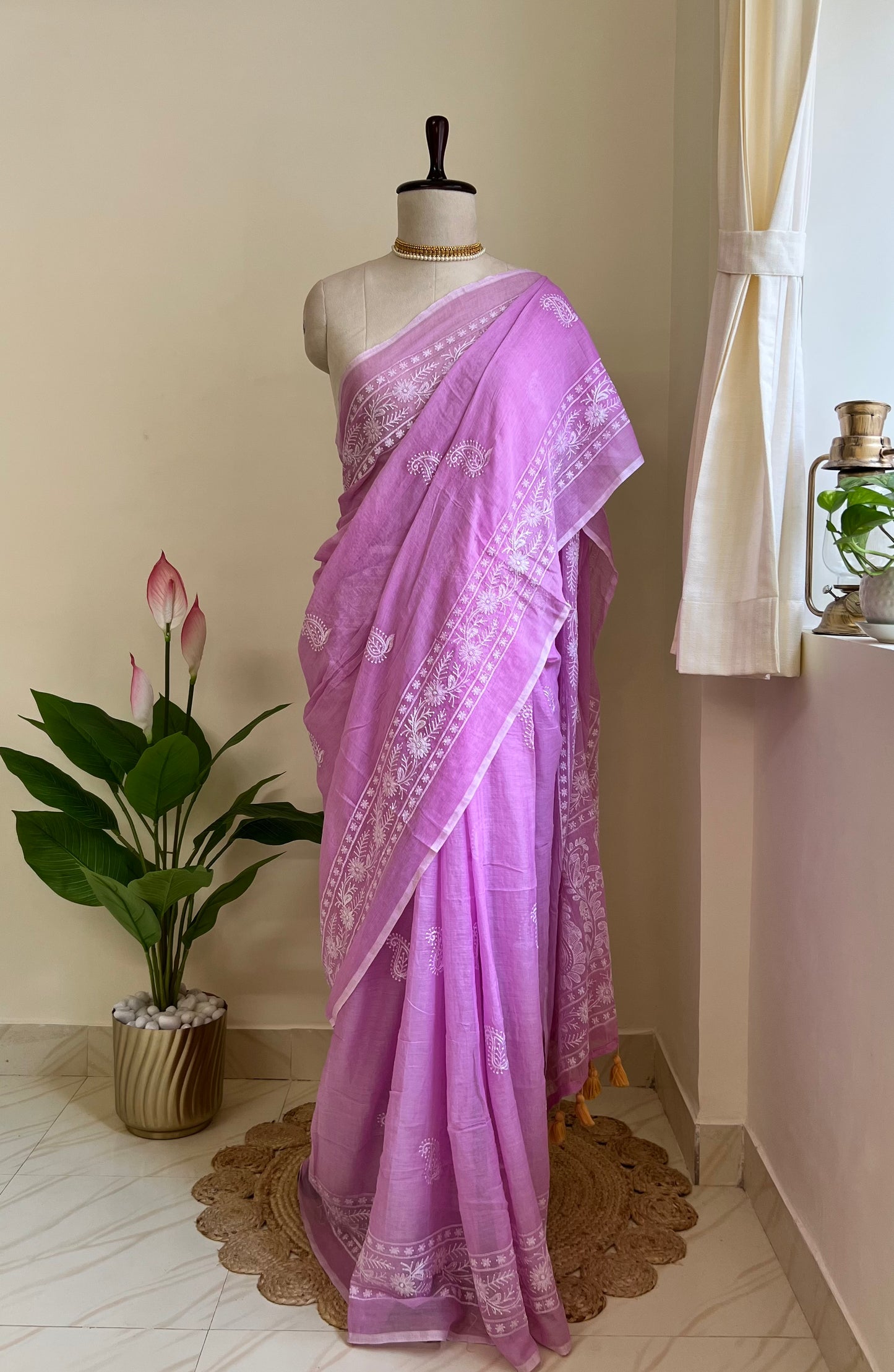 Lilac mul cotton saree with white chikankari-style embroidery, draped on a mannequin near a sunlit window