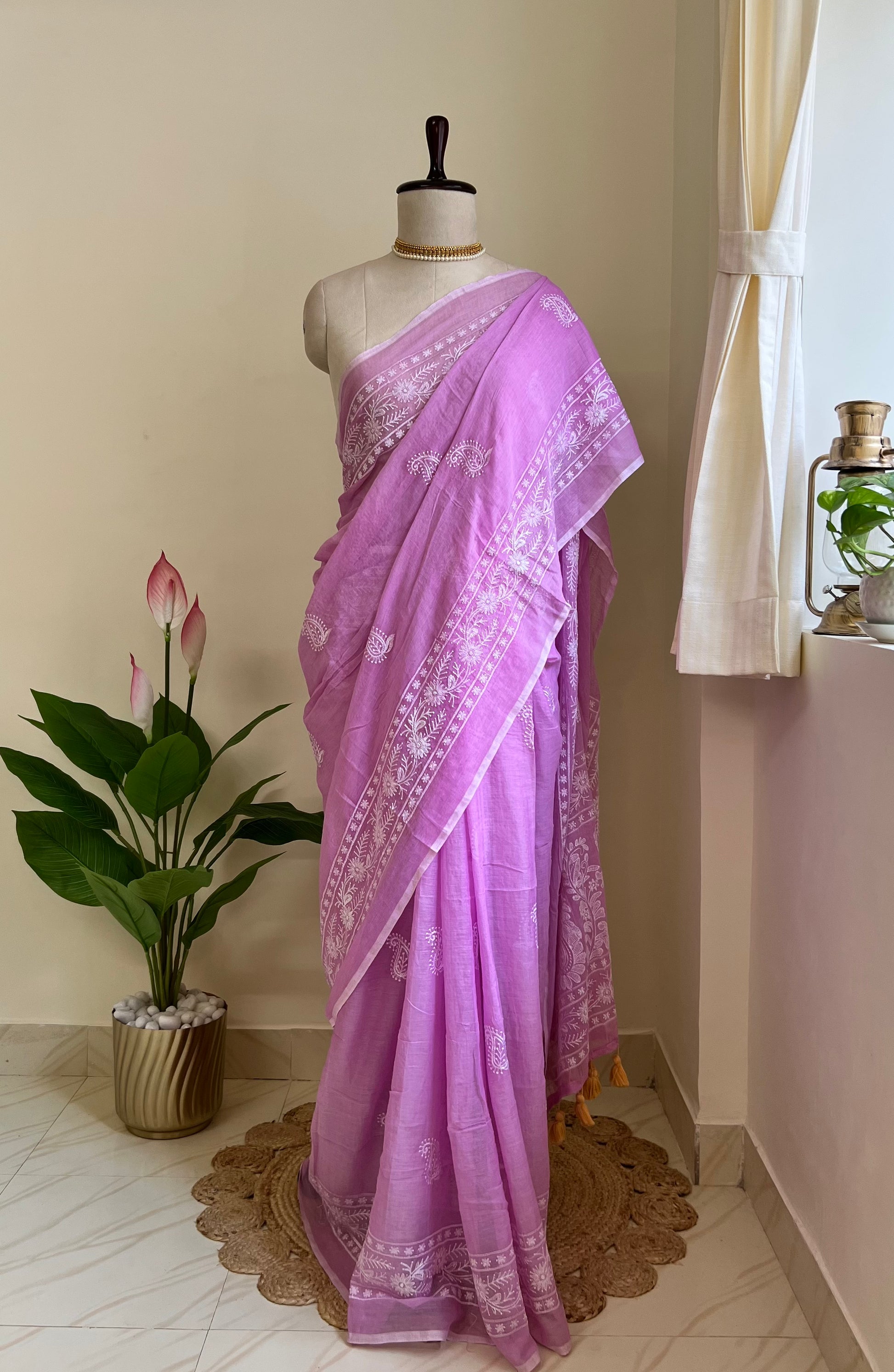 Lilac mul cotton saree with white chikankari-style embroidery, draped on a mannequin near a sunlit window