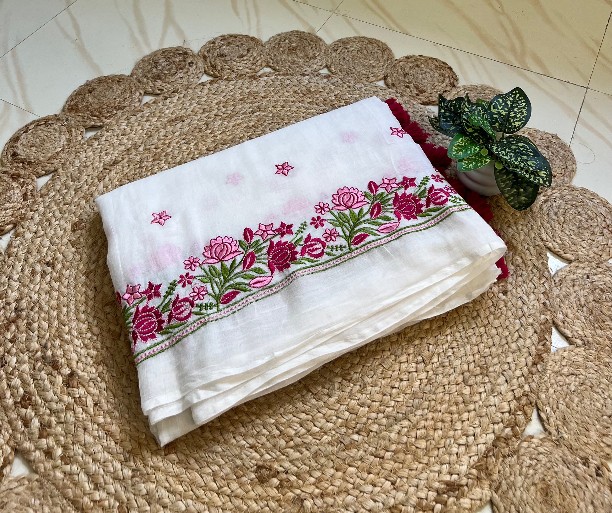 Folded white mul cotton saree showing pink and maroon floral embroidered border