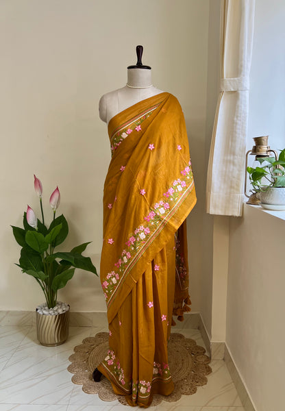 Mustard mul cotton saree with pink floral hand-embroidered border, draped on mannequin