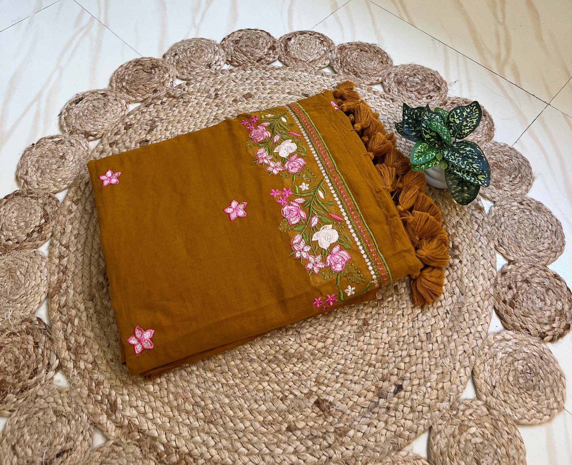Mustard mul cotton saree with pink floral embroidered border, neatly folded
