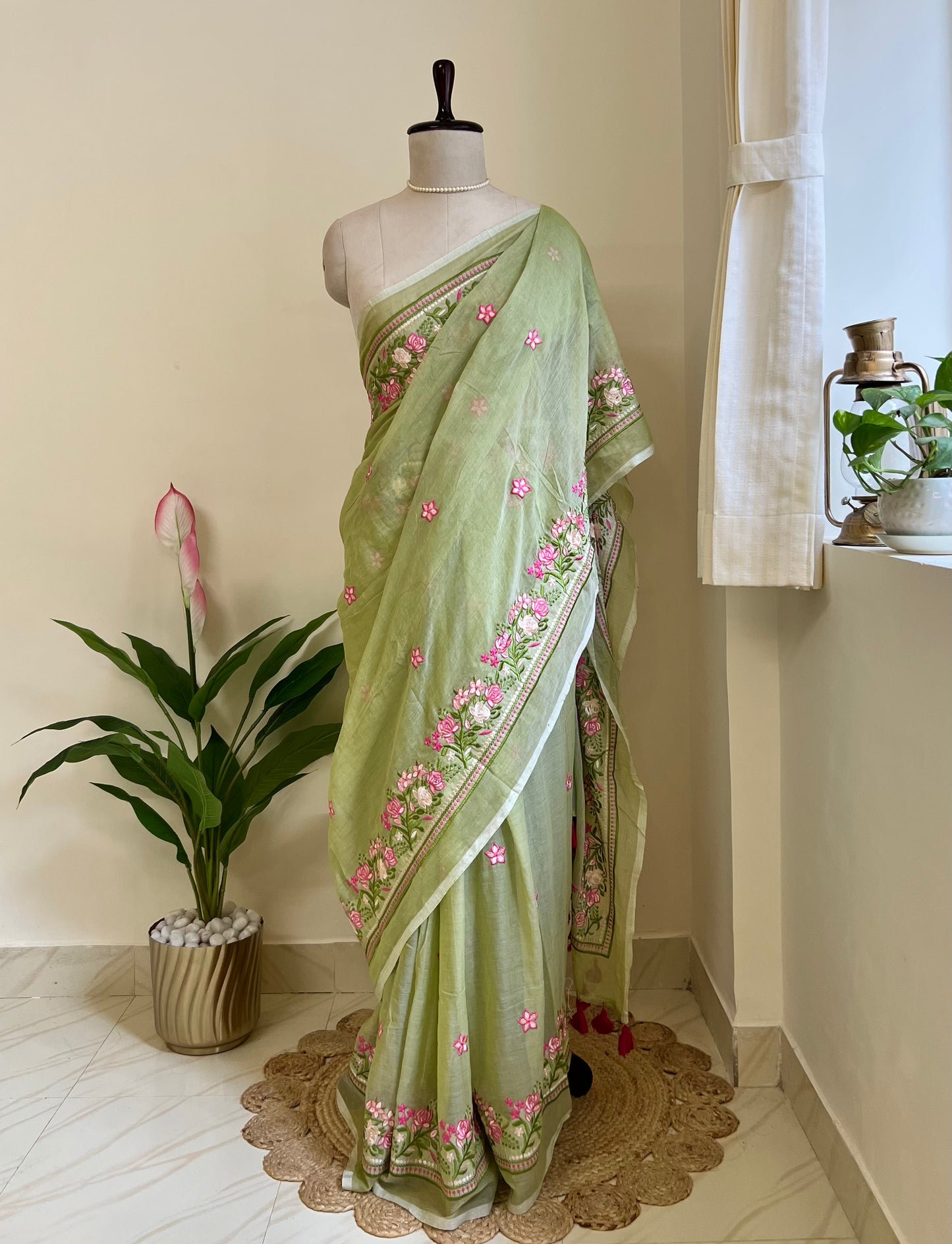 pista green mul cotton saree with pink hand-embroidered floral border, draped on a mannequin against a cream wall