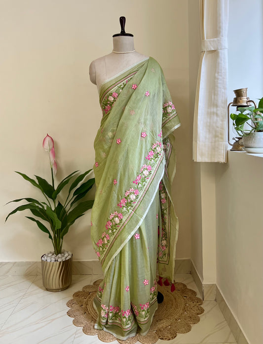 pista green mul cotton saree with pink hand-embroidered floral border, draped on a mannequin against a cream wall