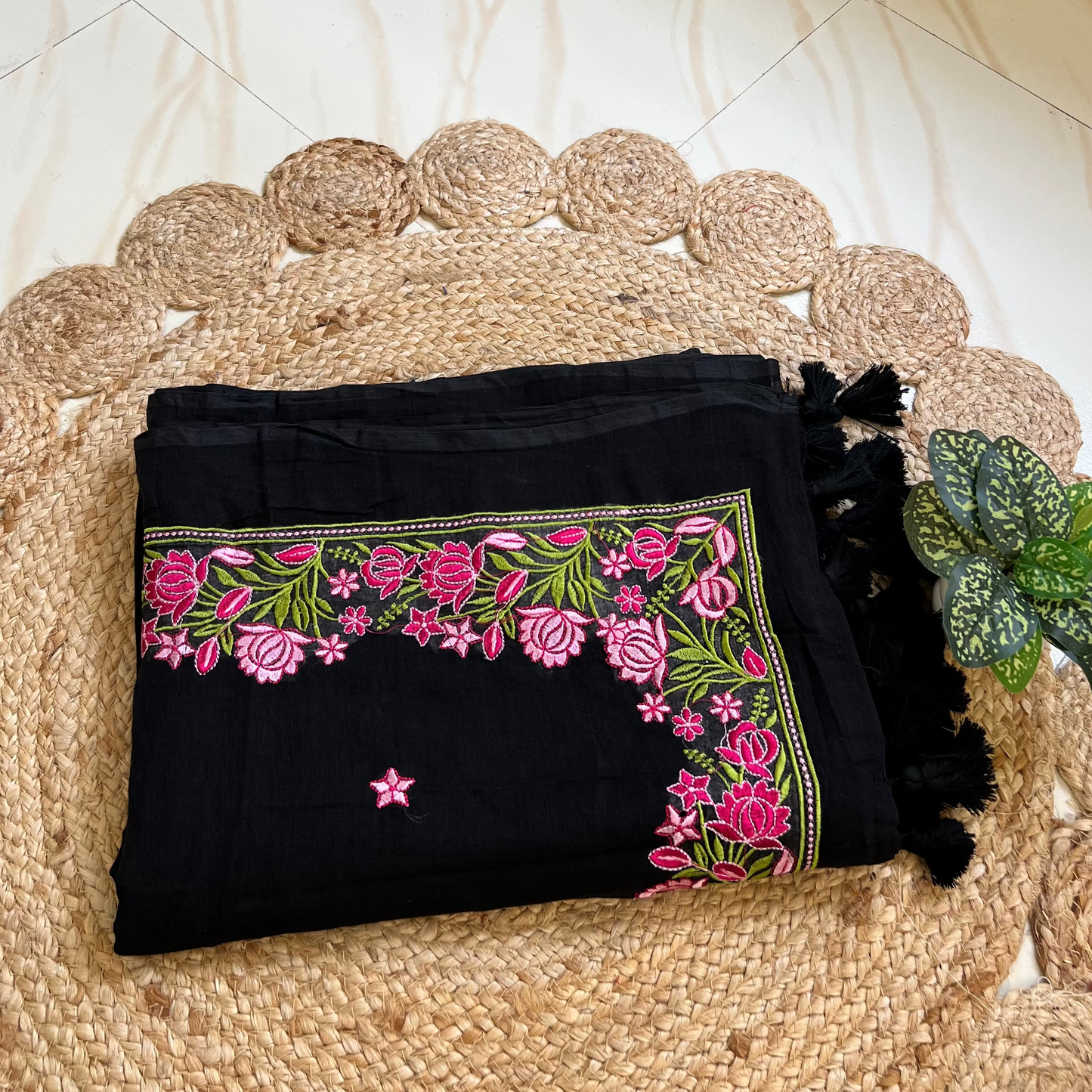 Folded black mul cotton saree showing pink floral embroidered border