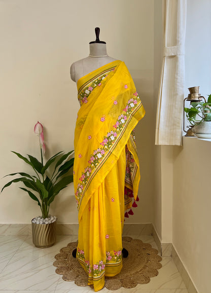 yellow mul cotton saree with pink and white embroidered floral border and tassel pallu, draped on a mannequin